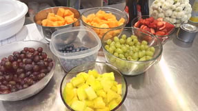 Bowls of fruit, including grapes, blueberries, pineapple pieces, strawberries, and cantaloupe.