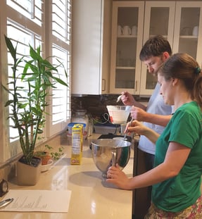 Jill mixes pancake batter in a bowl as Doug pours the first batch of batter on the griddle.