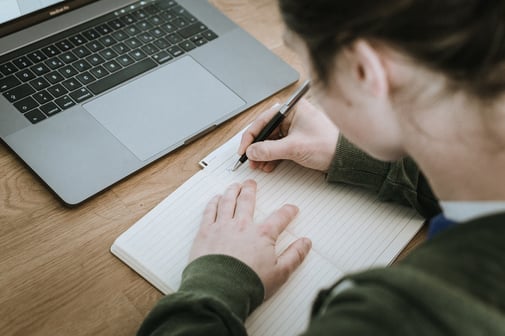 Student studying at table with laptop and notebook. 