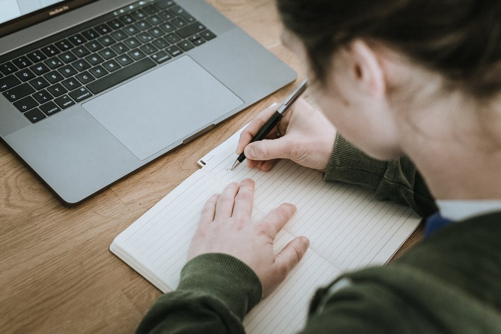 Student studying at table with laptop and notebook. 