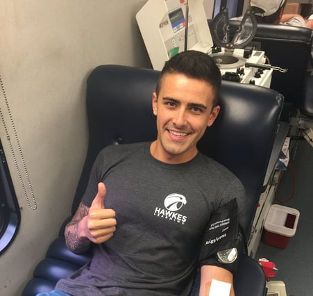A man holds a thumbs up sign as he sits while donating blood.