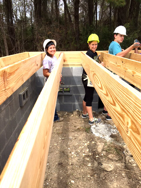 Venessa and Laura have hard hats on and help lay boards on top of the foundation.