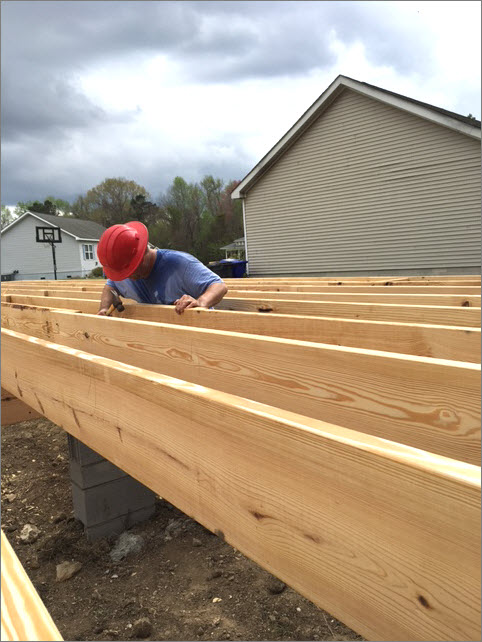 Jeff inspects the wooden board before hammering a nail.