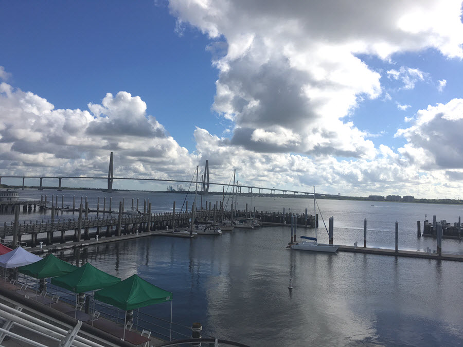 View of the Ravenel Bridge across the water underneath a cloudy sky.