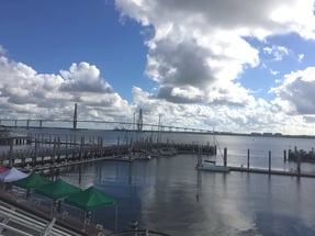 View of the Ravenel Bridge across the water underneath a cloudy sky.