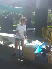 A woman in sunglasses pushes a pushcart topped with boxes.