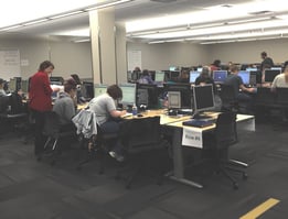 The picture shows a lab of about a hundred computers on several desks with students doing work.