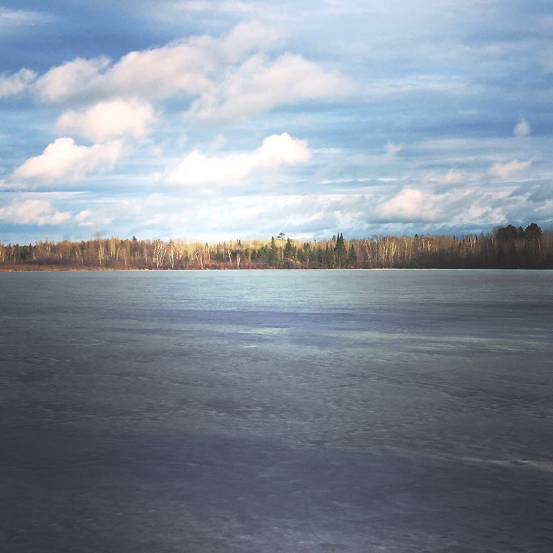 Frozen lake in Minnesota in front of a quiet wooded area.