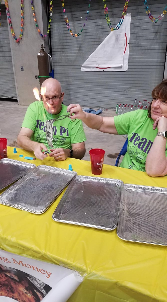 Volunteers hold a flaming dollar bill away from themselves in a fun experiment.