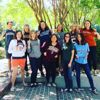 Eleven of Hawkes Learning's best and brightest employees stand outside wearing their college shirts.