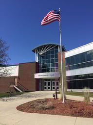 The front entrance to Riverland Community College underneath a perfect blue sky and next to an American flag waving proudly in the breeze.