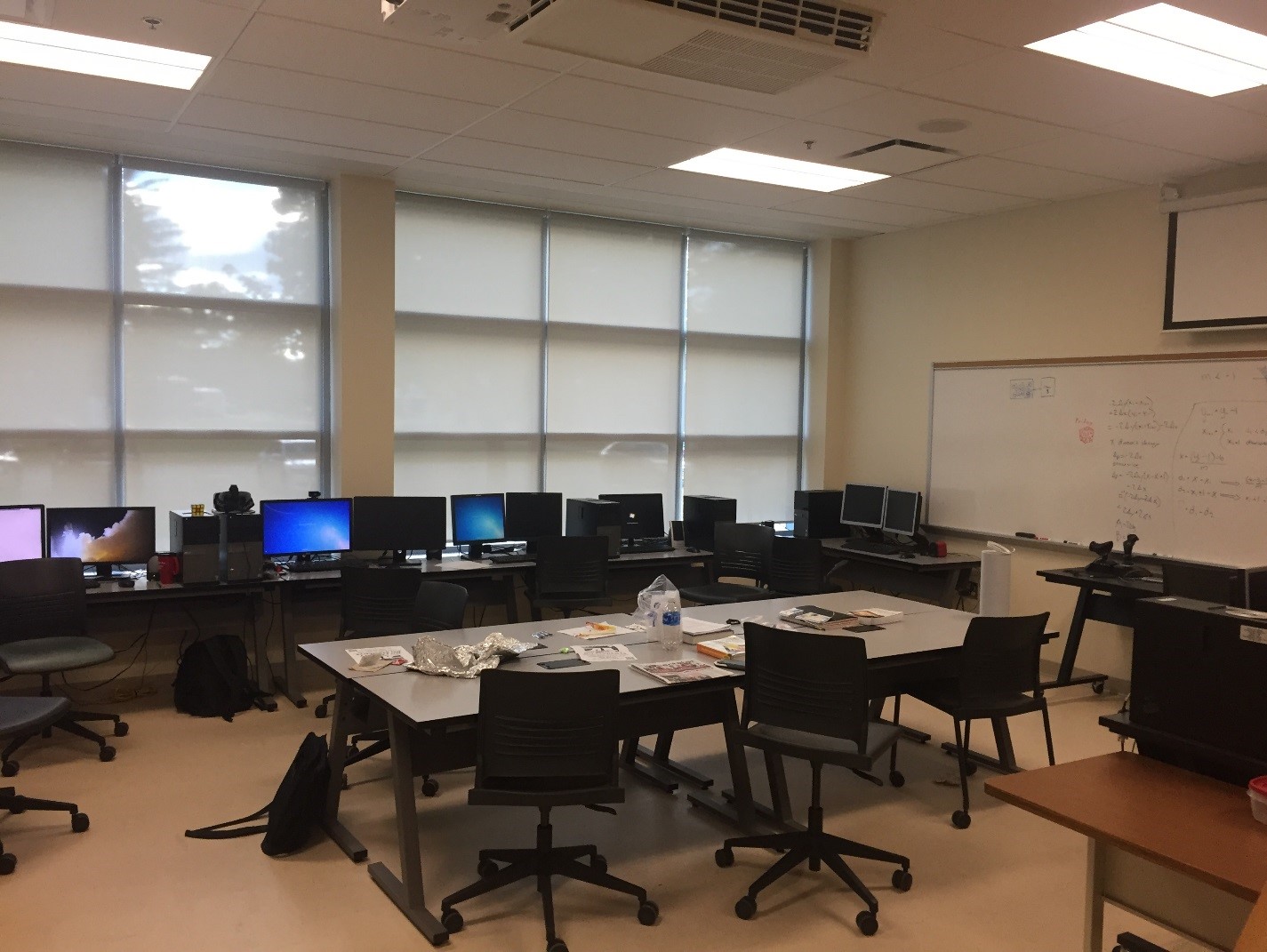 A computer lab with a long table in the middle and a white board on the furthest wall is shown.