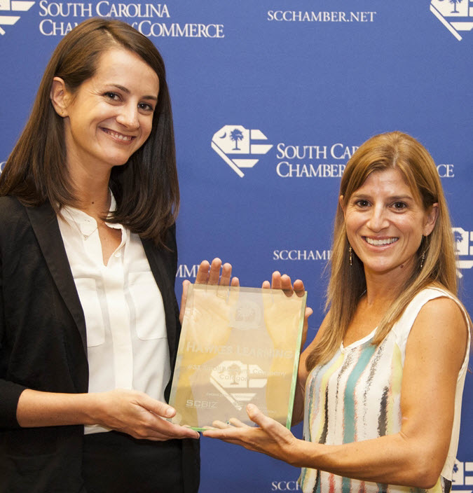 Two women stand smiling and holding a plaque that names Hawkes one of the best places to work in the state.
